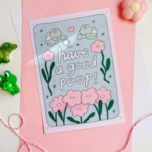 Load image into Gallery viewer, This image features a whimsical and charming wall print titled "Have a Good Poop!" Ideal for adding a playful touch to bathrooms, this print depicts a cheerful frog sitting atop a toilet, surrounded by vibrant pink flowers and lush green foliage. The phrase "have a good poop!" is prominently displayed in a friendly, handwritten-style font, enhancing the lighthearted and fun atmosphere of the artwork.
